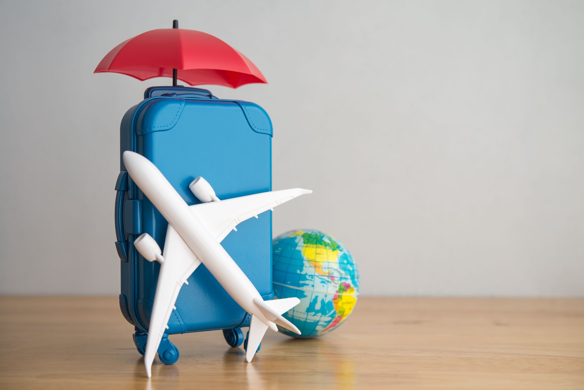 Umbrella, travel suitcase, airplane and globe on wooden table copy space.