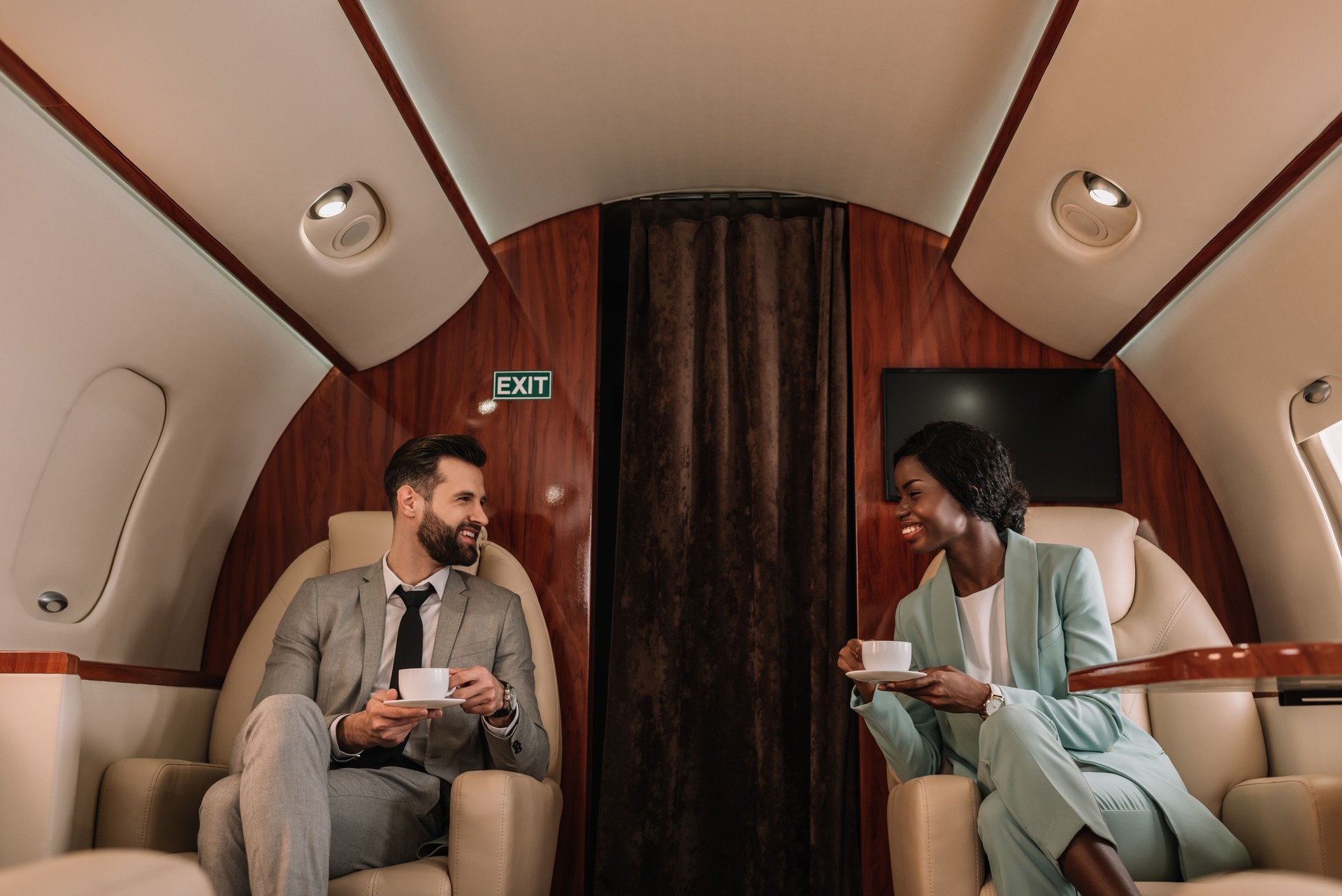 two smiling multicultural businesspeople talking while holding cups of coffee in plane two smiling multicultural businesspeople talking while holding cups of coffee in plane